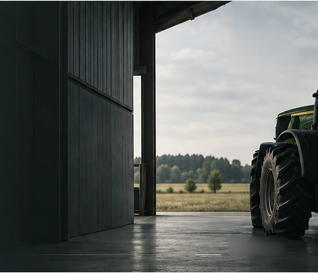 Green tractor standing in an open barn doorway, looking out over farmland